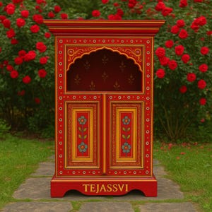 May include: A vibrant red cabinet with intricate yellow and blue floral designs. The cabinet features a decorative arched top and double doors. The word "TEJASSVI" is printed on the base. The cabinet is set against a backdrop of red roses.