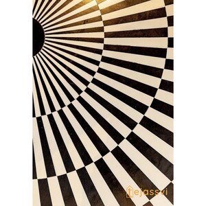 Op de afbeelding: Close-up van een zwart-wit patroon. Het ontwerp heeft een radiaal patroon met afwisselende zwarte en witte strepen, waardoor een geometrisch en optisch illusie-effect ontstaat. Het patroon doet denken aan een zonnestraal of een doel.