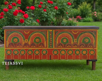 May include: A hand-painted wooden chest with a dark brown top and red base. The chest features intricate yellow, green, and red geometric designs. The chest is on short, dark brown legs and the text "TEJASSVI" is visible on the front.
