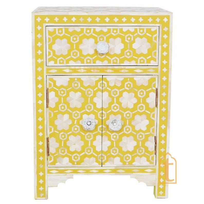 May include: A yellow and white nightstand with a floral pattern. The nightstand has a drawer and a cabinet with two doors. The drawer and cabinet doors have white, flower-shaped knobs. The nightstand is approximately 24 inches tall.