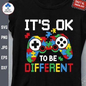 May include: A black t-shirt with a colorful puzzle piece design in the shape of a video game controller. The text "IT'S OK TO BE DIFFERENT" is printed below the controller.