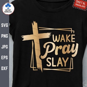 Op de afbeelding: Een zwart T-shirt met een gouden kruis en de tekst "WAKE PRAY SLAY" in een gouden kader.