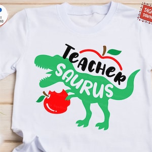 May include: A white t-shirt with a green dinosaur silhouette biting into a red apple. The text "Teacher Saurus" is written in black letters around the apple.