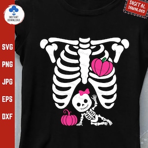Può includere: T-shirt nera con un disegno di scheletro bianco, un cuore e una zucca rosa. È incluso anche un piccolo scheletro con un fiocco e una zucca rosa. La scritta "DIGITAL DOWNLOAD" si trova in alto a destra.