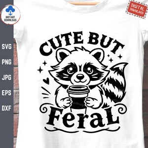 May include: Black and white illustration of a cute raccoon holding a cup of coffee. The text "Cute But Feral" is written above the raccoon.