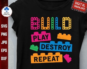 以下が含まれることがあります： 黒いTシャツに、カラフルなデザインが施されています。「BUILD PLAY DESTROY REPEAT」という文字がブロックのようなフォントで書かれています。デザインはブロック玩具を連想させます。