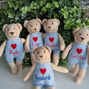 Könnte beinhalten: Fünf Plüschbären, die blaue und weiße gestreifte Latzhosen mit roten Herzen und personalisierten Namen tragen. Die Namen sind Paula, Leni, Marlen, Leni Malia und Frederik.