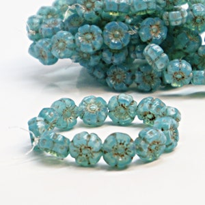 May include: A strand of turquoise blue glass flower beads. The beads are small and have a slightly iridescent finish.