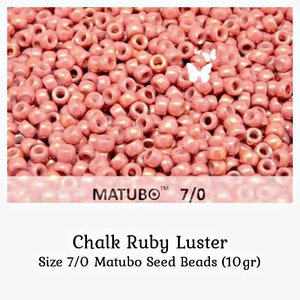May include: A collection of small, round, pinkish-red seed beads with a luster finish. The text MATUBO 7/0 is visible on the image. Below the image, the text reads Chalk Ruby Luster, Size 7/0 Matubo Seed Beads (10gr).