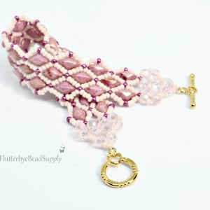 May include: A handmade bracelet featuring a diamond pattern of pink and white beads. The bracelet has a gold-colored toggle clasp and a delicate, beaded extension. The design incorporates small purple beads for added detail.