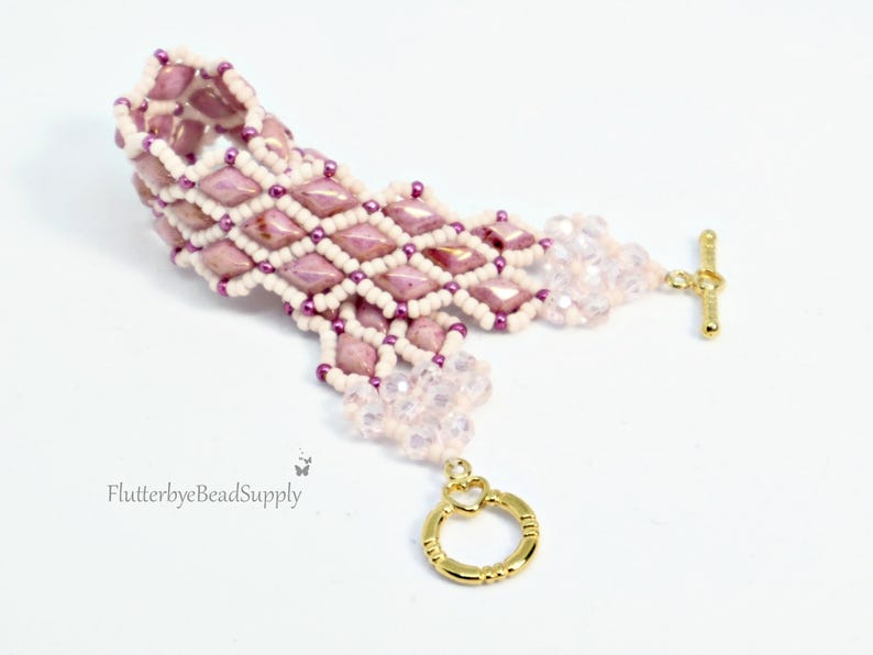 May include: A handmade bracelet featuring a diamond pattern of pink and white beads. The bracelet has a gold-colored toggle clasp and a delicate, beaded extension. The design incorporates small purple beads for added detail.