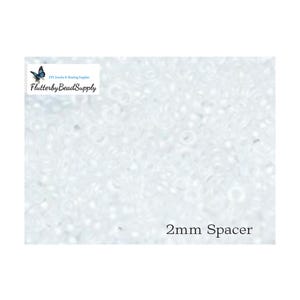 May include: Close-up of a collection of small, white spacer beads. The beads are 2mm in size and are used for DIY jewelry and beading supplies. The text "2mm Spacer" is visible.