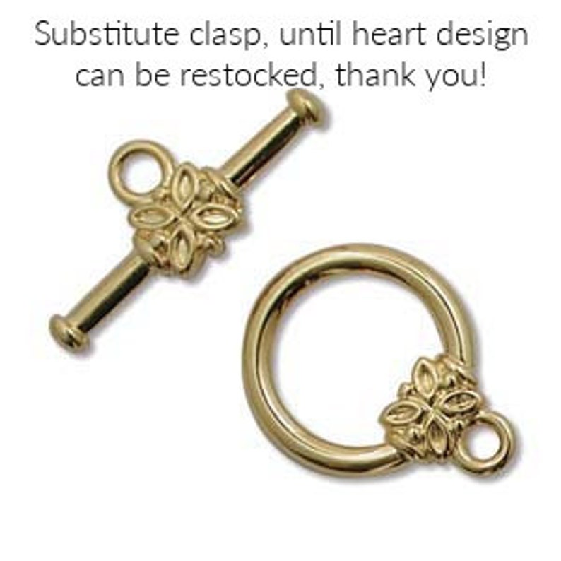 May include: Gold-colored toggle clasp with a floral design. The clasp includes a bar and a ring, both featuring decorative floral elements. The text in the image reads: Substitute clasp, until heart design can be restocked, thank you!