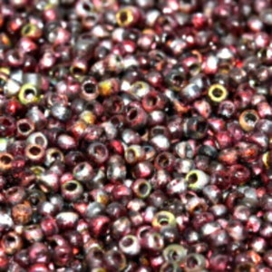 May include: Close-up of a pile of small, round beads in shades of burgundy, silver, and gold. The beads have a metallic sheen and are densely packed together, creating a textured surface. Ideal for jewelry making and crafts.