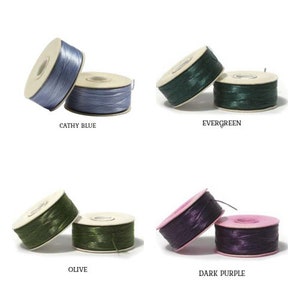 May include: Four spools of thread in shades of blue, green, and purple. The colours are labelled: Cathy Blue, Evergreen, Olive, and Dark Purple. The spools are on a white background.