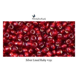 May include: Close-up of silver-lined ruby beads. The beads are a deep red color with a silver lining, creating a reflective quality. The image includes the text "Silver Lined Ruby #25c" and the FlutterbyBeadSupply logo.