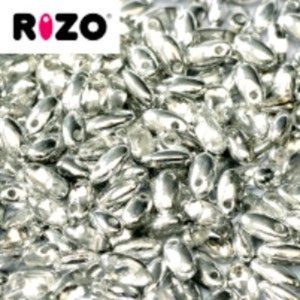 May include: A large collection of small, metallic silver-colored oval beads with a smooth, reflective finish. Each bead features a single hole for threading. The brand name ROZO is printed in black and pink text in the upper left corner.