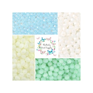 May include: An assortment of faceted beads in various colors, including light blue, white, pale yellow, and mint green. The image also features a logo with the text "Flutterby Bead Supply" surrounded by butterflies and flowers.