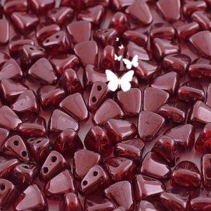 May include: A close-up of a pile of small, dark red, triangular glass beads with two holes each. The beads have a shiny, iridescent finish.