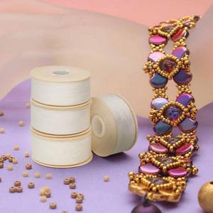May include: A decorative bracelet with gold-tone metalwork and iridescent purple, blue, and pink beads. Three rolls of white ribbon are stacked beside a single roll. Small wooden beads are scattered on a purple surface.