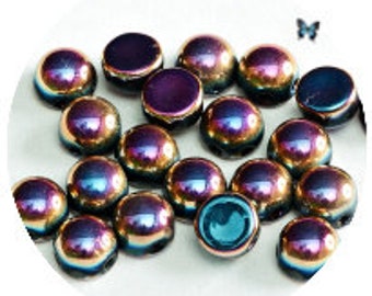 Könnte beinhalten: Eine Sammlung von irisierenden, kuppelförmigen Glasperlen mit metallischem Glanz. Die Perlen zeigen eine Reihe von Farben, darunter Blau, Lila und Gold. Sie sind auf einer weißen Oberfläche angeordnet, mit einem kleinen Schmetterling im Hintergrund.