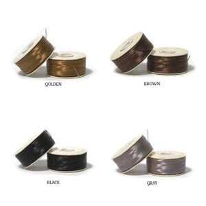 May include: Four pairs of thread spools in golden, brown, black, and grey. Each pair has one spool upright and one lying down. The colours are labelled below each pair of spools.