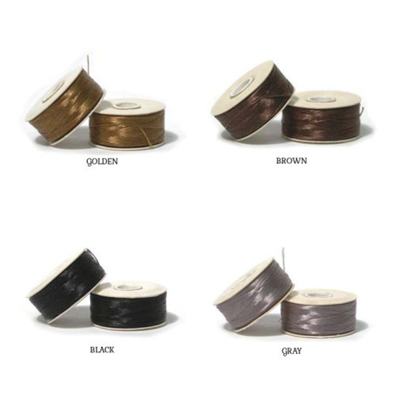 May include: Four pairs of thread spools in golden, brown, black, and grey. Each pair has one spool upright and one lying down. The colours are labelled below each pair of spools.