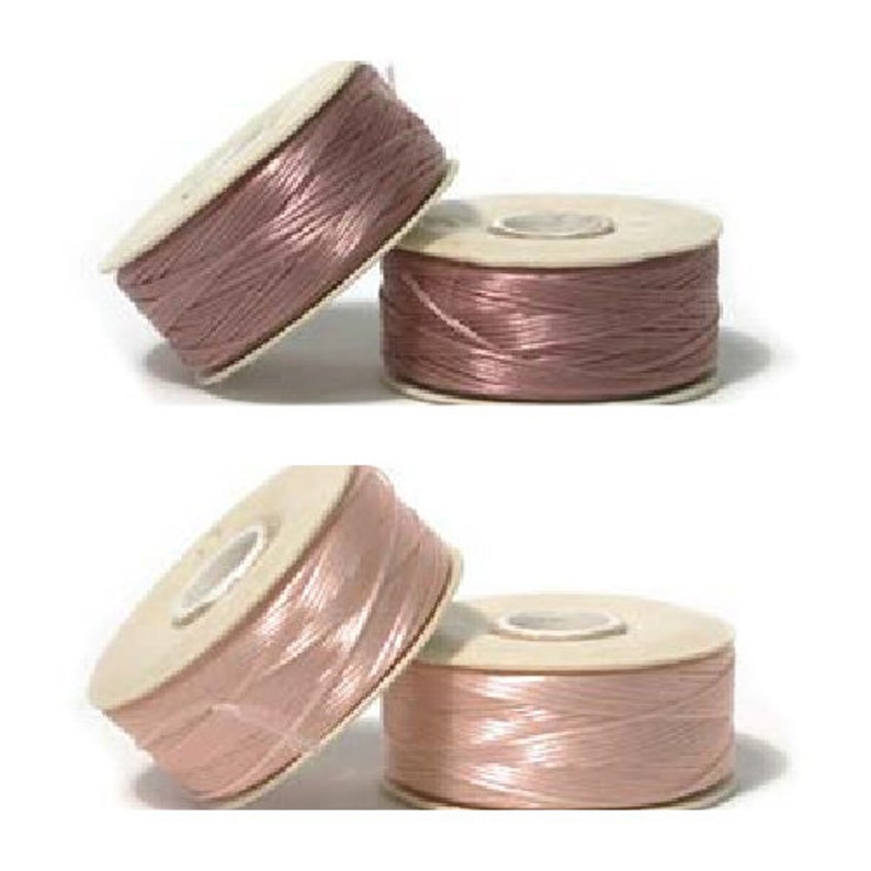 May include: Four spools of satin cord in shades of pink and mauve. The cord is tightly wound on cardboard spools. The spools are arranged in a group, with some tilted and others upright. The cord has a slight sheen.