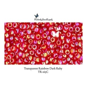 May include: A collection of small, round, transparent ruby red glass seed beads with an iridescent rainbow finish. The text "FlutterbyBeadSupply" and "Transparent Rainbow Dark Ruby TR-165C" is printed above and below the bead cluster.