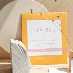 K&ouml;nnte beinhalten: Eine gelbe und wei&szlig;e Verpackung von Ollie Belle Cover Dot Acne Care. Die Verpackung zeigt ein rosafarbenes Logo mit einer Flasche und dem Text "Ollie Belle". Der Text "Cover Dot Acne Care" ist in Schwarz. Die Verpackung enth&auml;lt au&szlig;erdem den Text "medikamentenfrei, nicht austrocknend, reduziert Narbenbildung, abgeschr&auml;gte Kanten, wasserdichter Schutz, 72 Punkte, FDA-registriert, hergestellt in den USA".