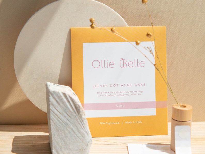 K&ouml;nnte beinhalten: Eine gelbe und wei&szlig;e Verpackung von Ollie Belle Cover Dot Acne Care. Die Verpackung zeigt ein rosafarbenes Logo mit einer Flasche und dem Text "Ollie Belle". Der Text "Cover Dot Acne Care" ist in Schwarz. Die Verpackung enth&auml;lt au&szlig;erdem den Text "medikamentenfrei, nicht austrocknend, reduziert Narbenbildung, abgeschr&auml;gte Kanten, wasserdichter Schutz, 72 Punkte, FDA-registriert, hergestellt in den USA".