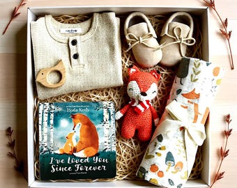 May include: A gift box containing a beige waffle-knit long-sleeve shirt, a pair of beige moccasins, a wooden bird-shaped teether, a crocheted orange fox toy, and a book titled I've Loved You Since Forever with a fox-themed swaddle blanket.