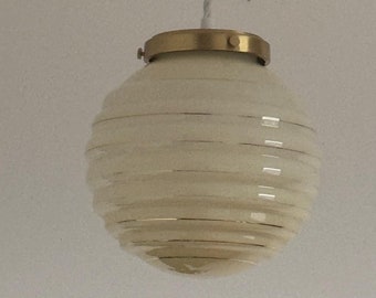 May include: A white glass pendant light with a brass fixture and a ribbed design. The light is hanging from a white cord.