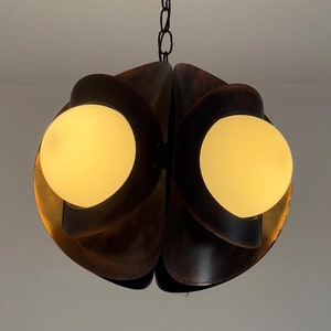 Puede incluir: Una l&aacute;mpara colgante de estilo moderno de mediados de siglo con un acabado marr&oacute;n oscuro de madera. La l&aacute;mpara tiene dos bombillas blancas en forma de globo.