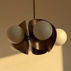 May include: A modern, mid-century style pendant light fixture with four white globe light bulbs and a bronze finish.