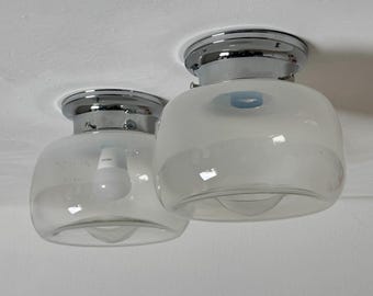 May include: Two flush mount ceiling light fixtures featuring polished chrome bases and rounded, frosted glass shades. Each fixture has a clear glass bottom section and a visible white light bulb inside the glass housing.