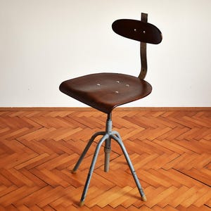 May include: A vintage industrial chair with a dark brown wooden seat and a metal backrest. The chair has a swivel base with three legs and is painted a light blue color.