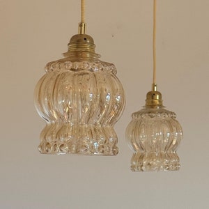 May include: Two clear glass pendant lights with a ribbed texture and a gold metal finish. The lights are hanging from a white cord.