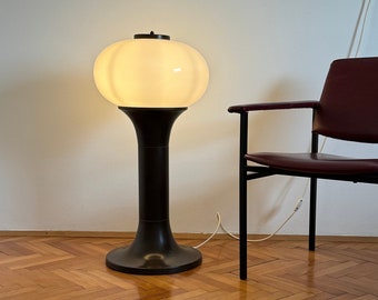 Könnte beinhalten: Eine Vintage-Stehlampe mit einem weißen, kugelförmigen Schirm und einem dunkelbraunen Stiel und Sockel. Daneben ein bordeauxroter Ledersessel mit schwarzem Rahmen. Der Boden ist aus Holz mit Fischgrätmuster.