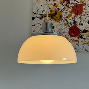 May include: A white frosted glass dome pendant light with a chrome finish. The light is hanging from a white cord and is illuminated with a warm white light bulb.