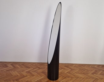 May include: A black floor mirror with an oval-shaped reflective surface. The mirror is standing on a wooden floor.