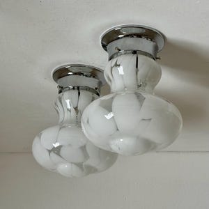 May include: Two ceiling-mounted light fixtures with chrome bases and white glass shades. The shades have a marbled pattern of white and gray. The fixtures are mounted on a white ceiling.