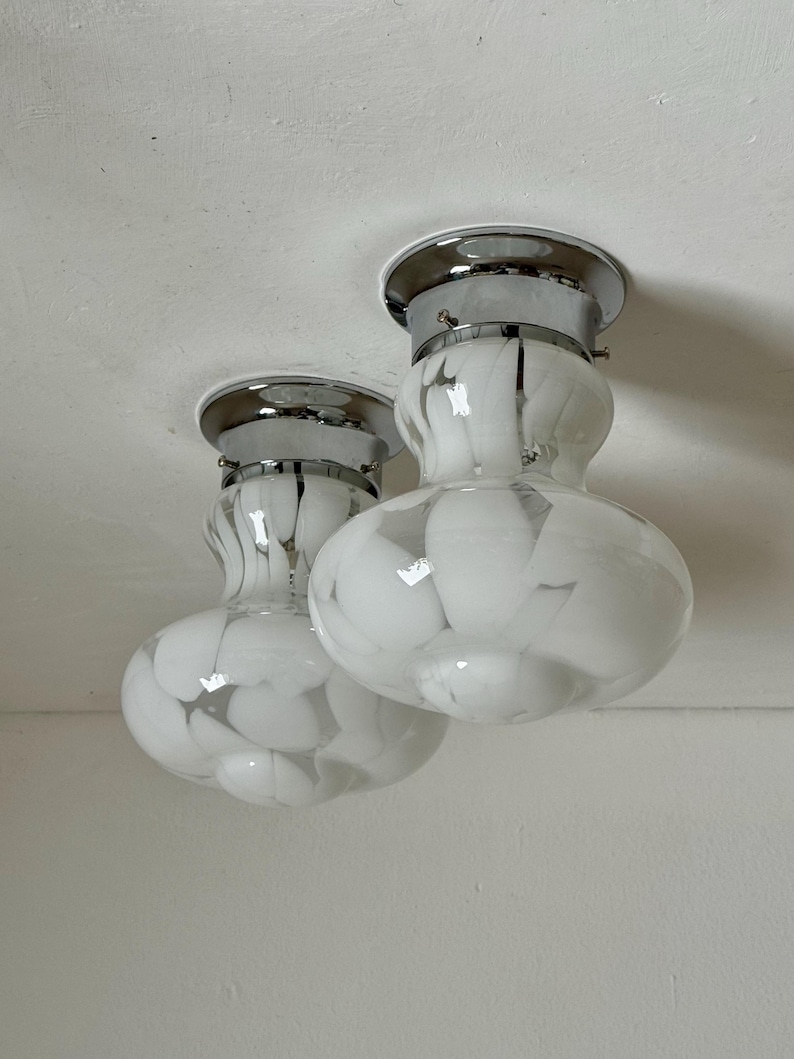 May include: Two ceiling-mounted light fixtures with chrome bases and white glass shades. The shades have a marbled pattern of white and gray. The fixtures are mounted on a white ceiling.