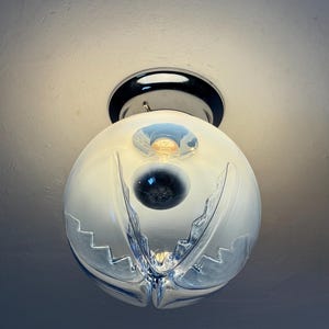 May include: A contemporary ceiling light. The spherical, frosted glass shade features a distinctive, layered design with a clear, cut-glass pattern. The fixture has a chrome base and a visible lightbulb.