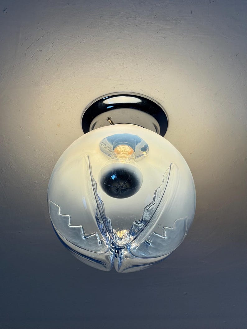 May include: A contemporary ceiling light. The spherical, frosted glass shade features a distinctive, layered design with a clear, cut-glass pattern. The fixture has a chrome base and a visible lightbulb.