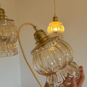 May include: Three clear glass pendant lights with gold metal fixtures. The lights have a ribbed design and are hanging from white cords.