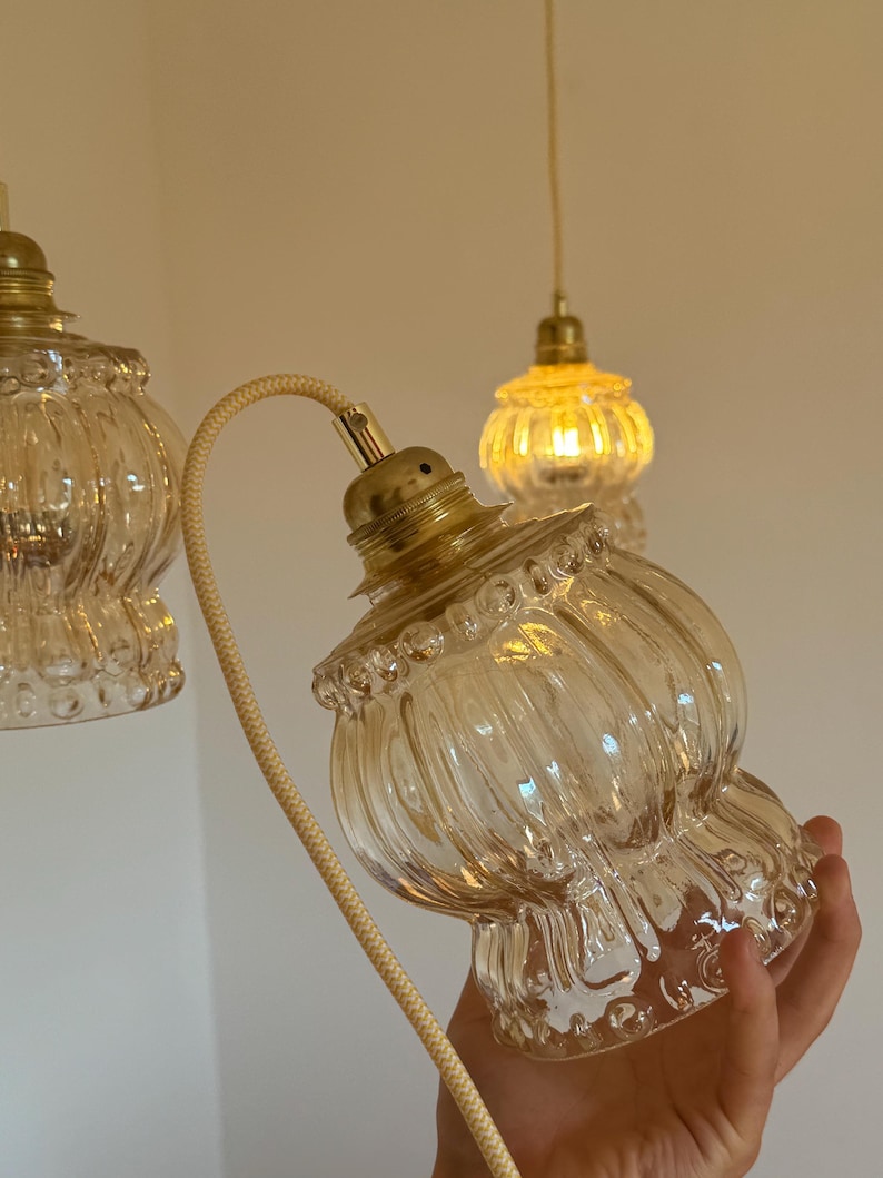 May include: Three clear glass pendant lights with gold metal fixtures. The lights have a ribbed design and are hanging from white cords.