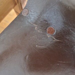 May include: Close-up of a brown leather surface with three copper-colored rivets. The leather has a worn, textured look.