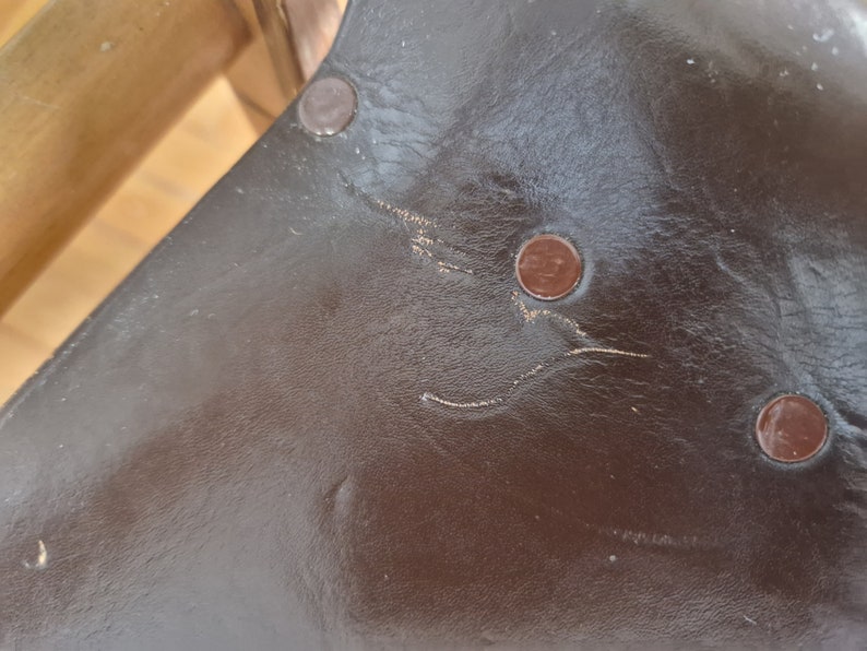 May include: Close-up of a brown leather surface with three copper-colored rivets. The leather has a worn, textured look.
