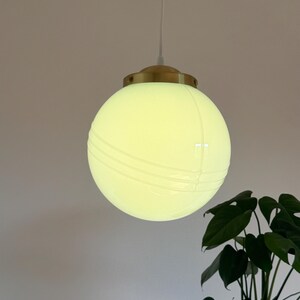 May include: A white globe pendant light with a brass fixture. The globe has a textured surface with lines running across it.